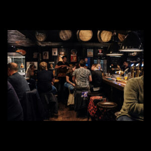  A warm and inviting scene inside a modern-day pub, showcasing people socializing, bartenders serving drinks, and rustic decor, encapsulating the enduring appeal of social venues throughout the evolution of nightlife.